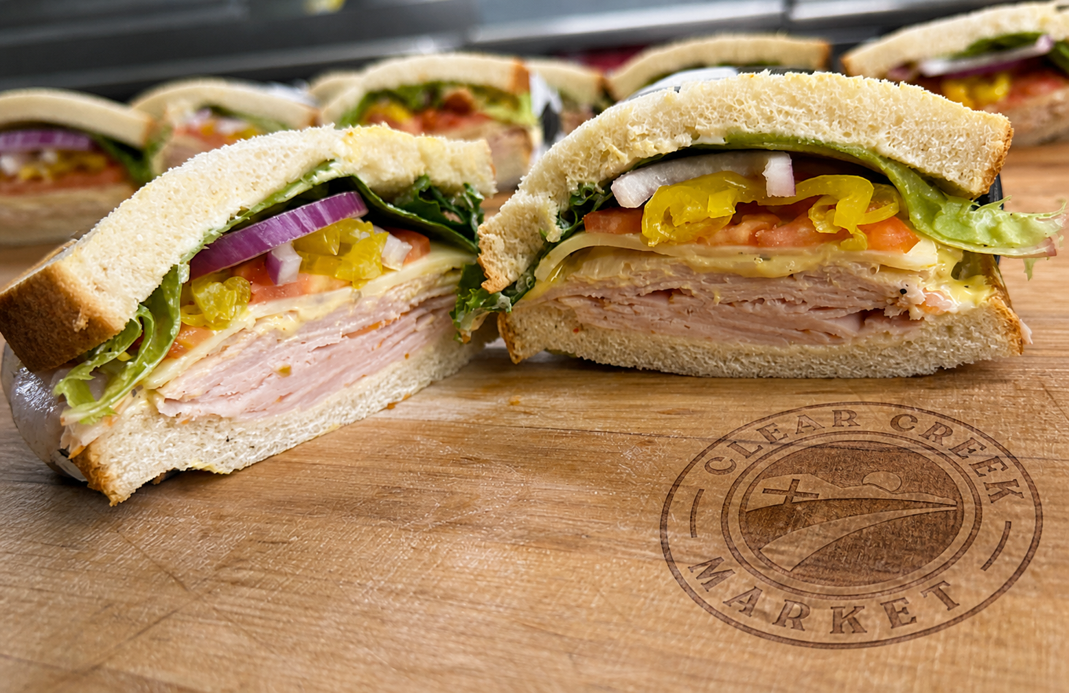 Fresh Clear Creek Market sandwiches beside the market logo branded into a wooden cutting board